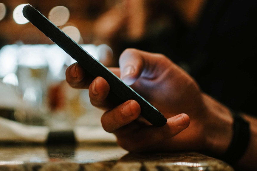 A male hand holds a mobile phone viewed from the side.