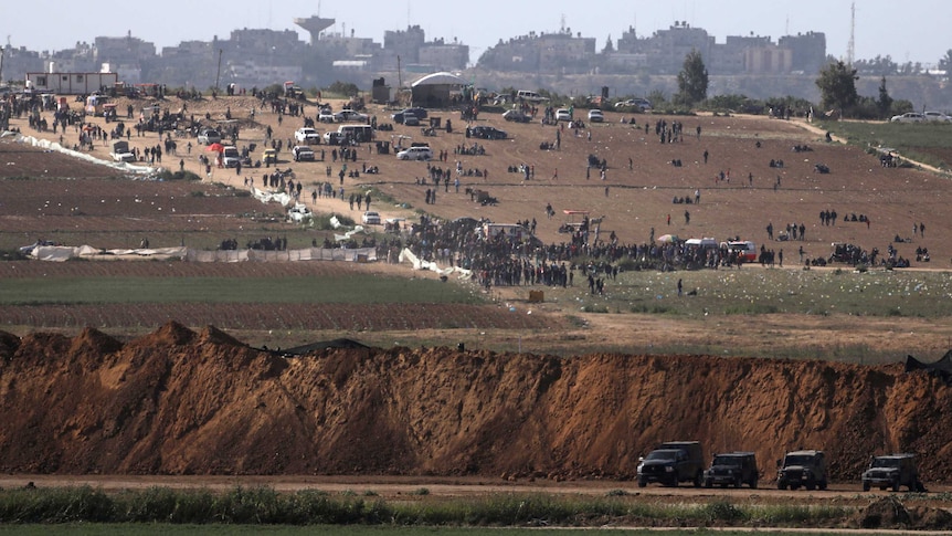 Israeli military vehicles on the Israeli side of the Israel-Gaza border, as Palestinians demonstrate on the Gaza side.