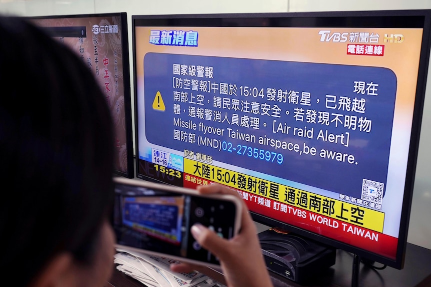 A person takes a photo of a screen showing English and Chinese writing.