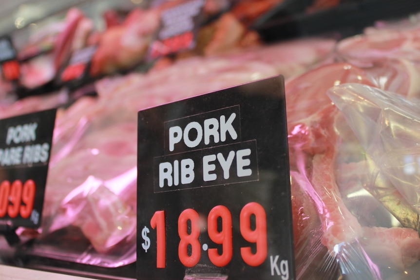 Close up shot of pork rib eye chops for sale in a butcher's window, labelled $18.99 per kilogram.