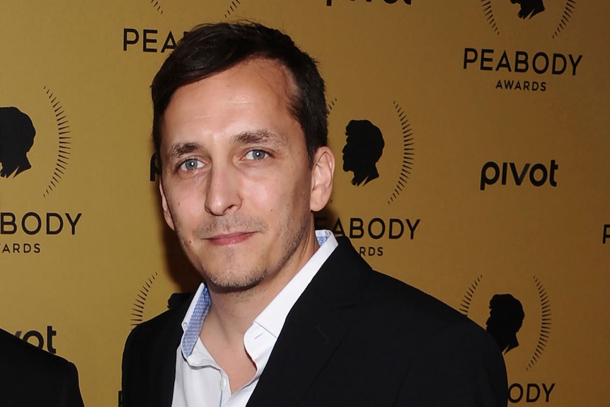 A man in a suit stands in front of a backdrop which says "peabody awards"