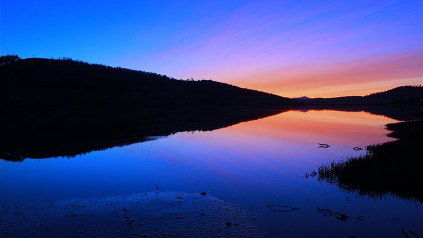 Bright blue sky with orange and pink colours near the horizon with the sky reflected in still water