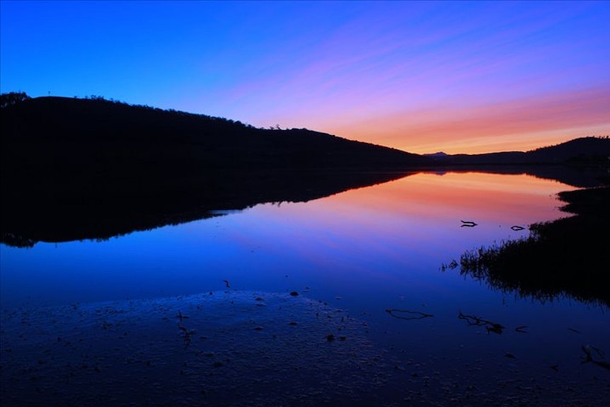 Bright blue sky with orange and pink colours near the horizon with the sky reflected in still water