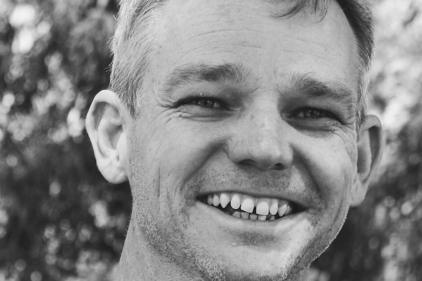 black and white portrait of Caucasian man with a big smile against leafy background