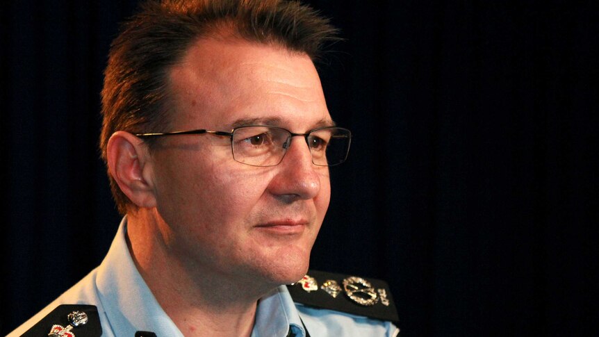 Side profile of AFP Commissioner Reece Kershaw, in a room with flags hanging behind him.