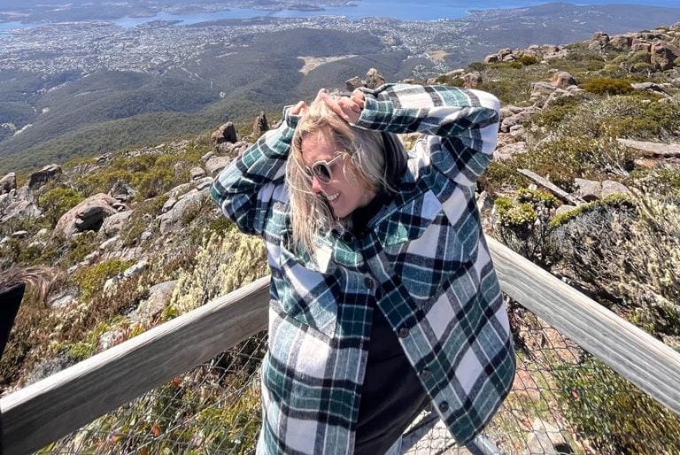 A woman with long blonde hair stands on top of a mountain