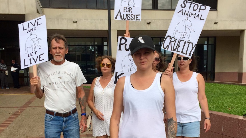 Jasmine Laird, who claims her ex-partner killed her pet dog 'Aussie', stands in front of four protestors holding placards