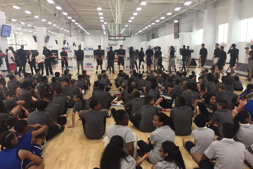 Ben Simmonds stands in front of a group of seated children with other NBA basketballers.