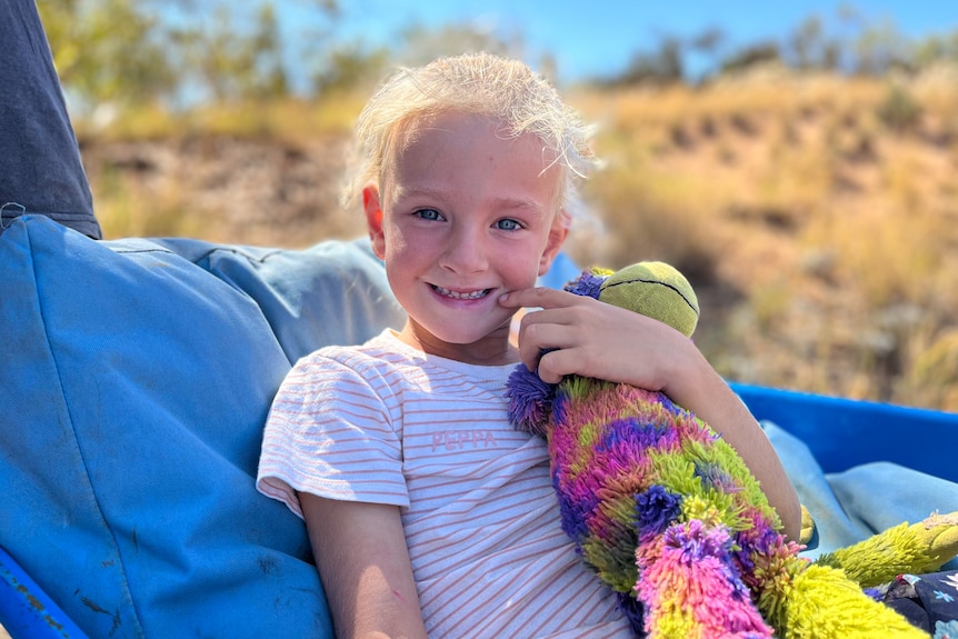 A six-year-old girl smiles while holding a colourful monkey toy.