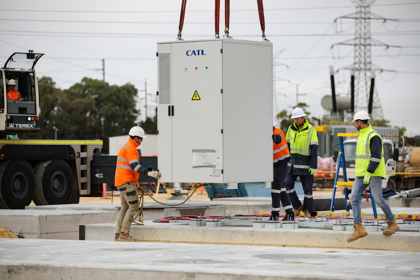 A white electrical box being hoisted into place by a crane 