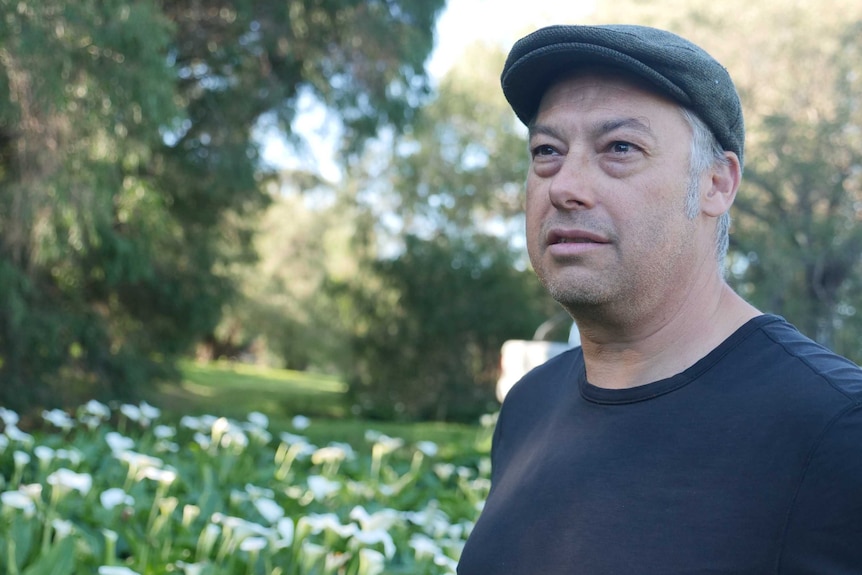 A man in a flat cap stands near arum lilies