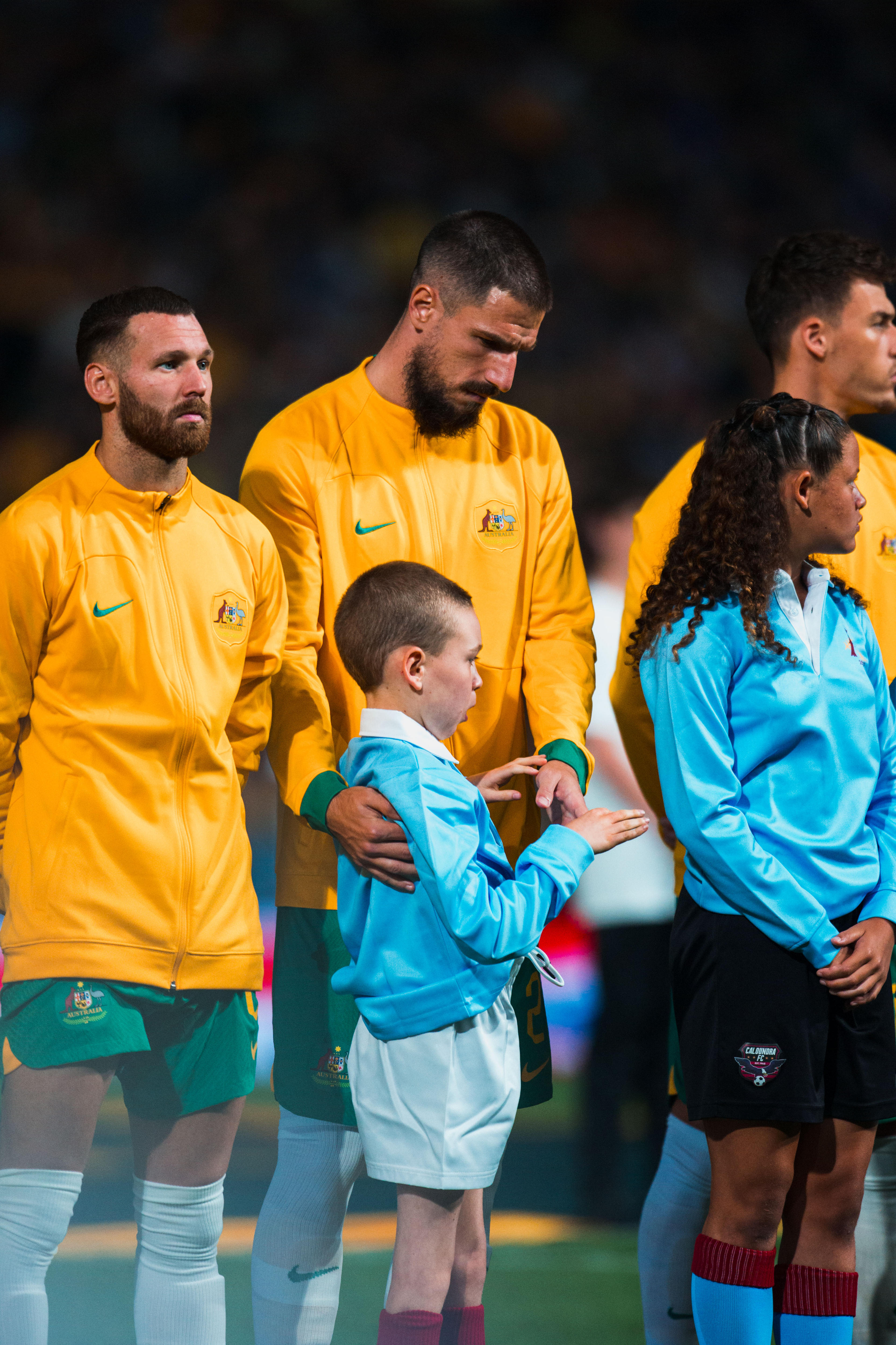 A soccer player wearing yellow holds his hands out to a young boy wearing blue before a game