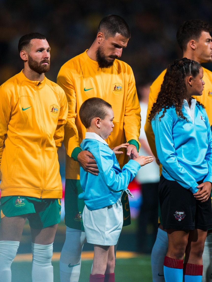 A soccer player wearing yellow holds his hands out to a young boy wearing blue before a game