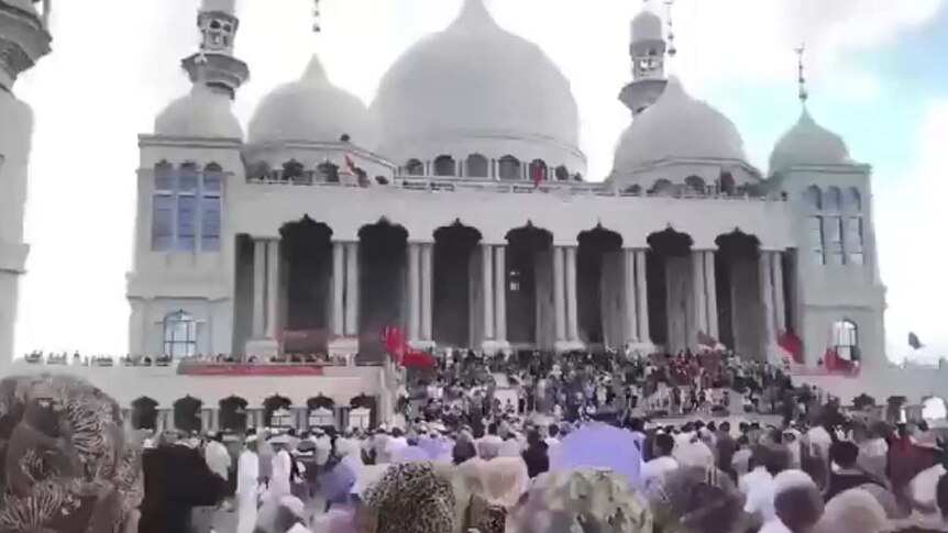 An image of a mass of people at the Weizhou Grand Mosque. It is a huge white building.