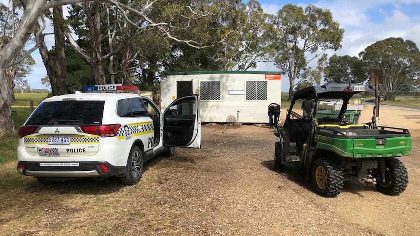 A police vehicle parked next to a farm buggy on a dirt road.