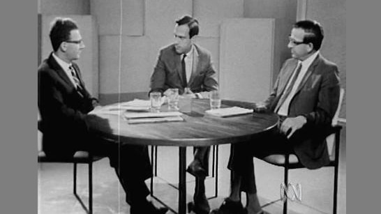 Three men sit around table in discussion