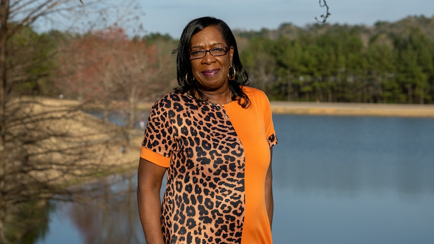 A woman in an orange shirt smiles for a photo near a lake 