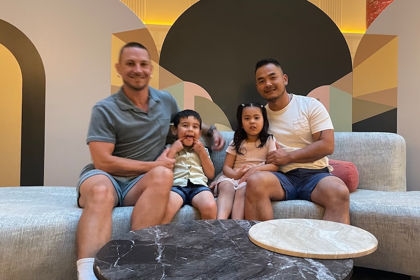 Two young men are sitting in sofa with children in their arms