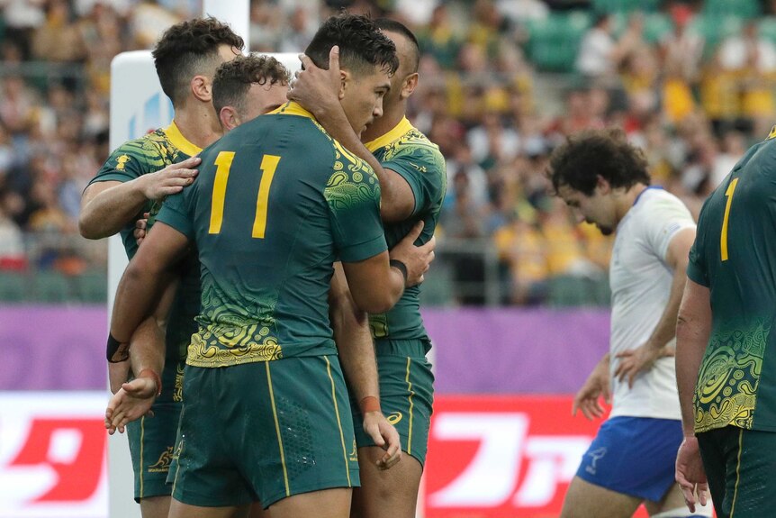 A Wallabies player is hugged by his teammates as he holds the ball after scoring a try at the Rugby World Cup.