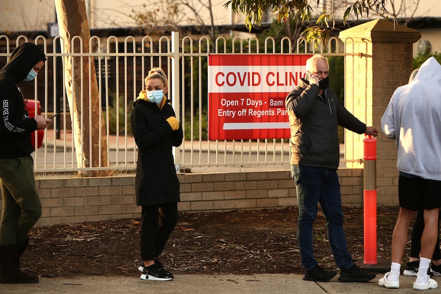People wearing face masks queue outside a COVID clinic at dawn.