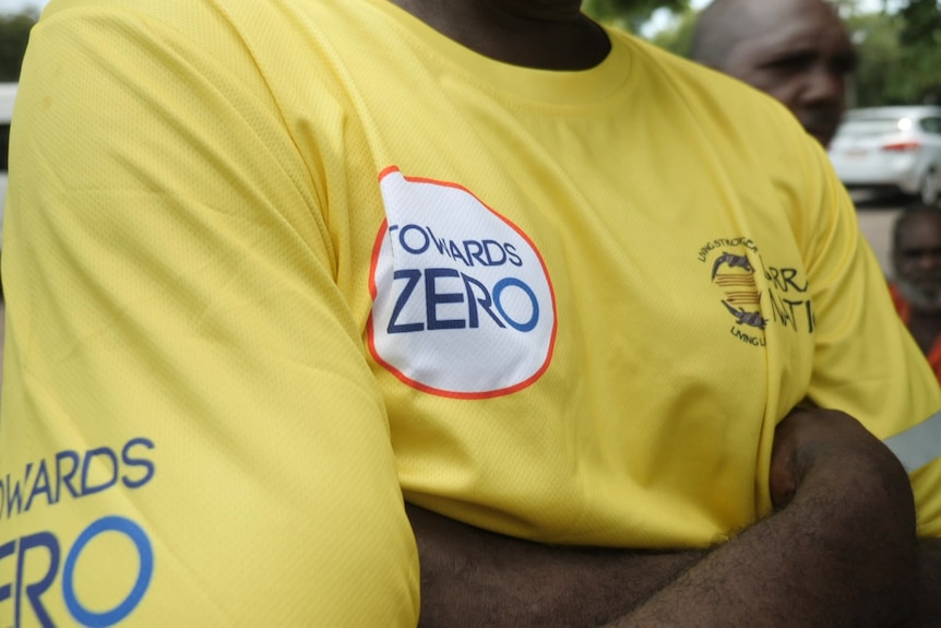 A photo of a man's torso. He has his arm's crossed and is wearing a yellow t-shirt