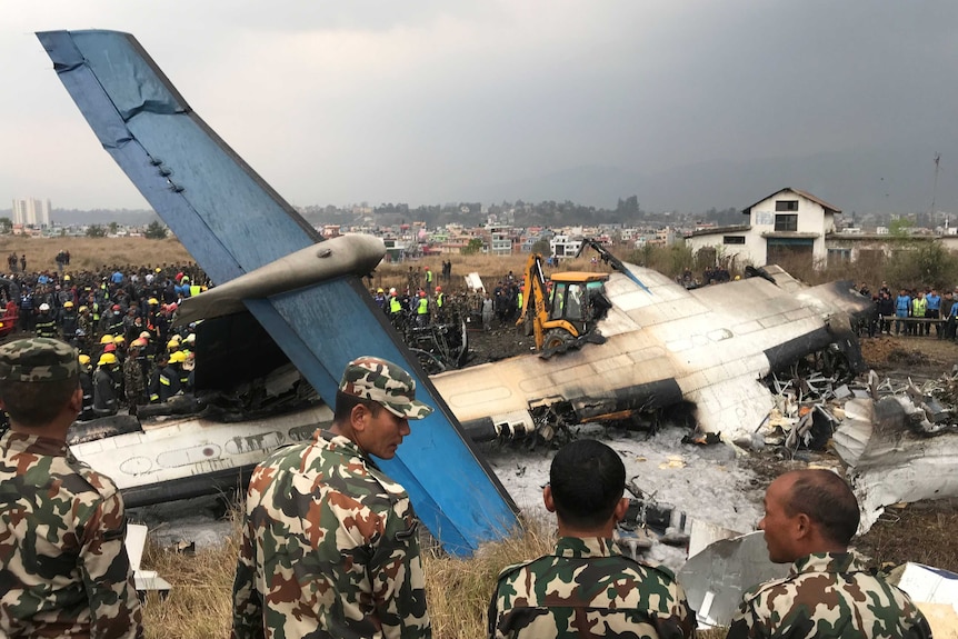 A badly wrecked and burned plane with its tail in the air is pictured with dozens of rescue workers next to it