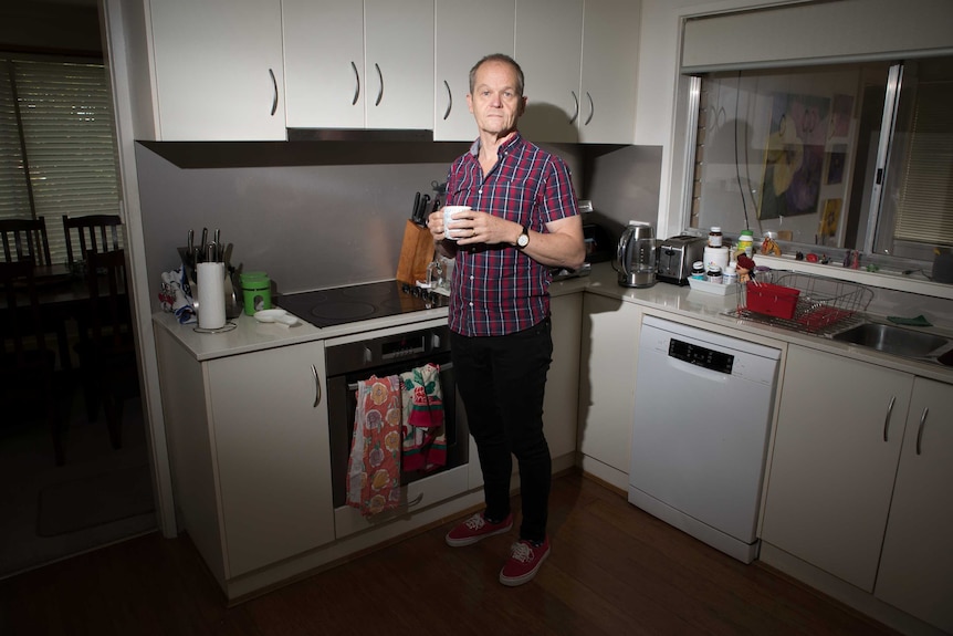 A man stands in a kitchen holding a cup.