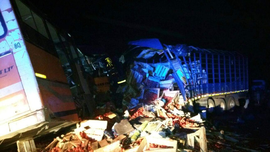 A picture of the bus crashed into the truck with tomato boxes everywhere.