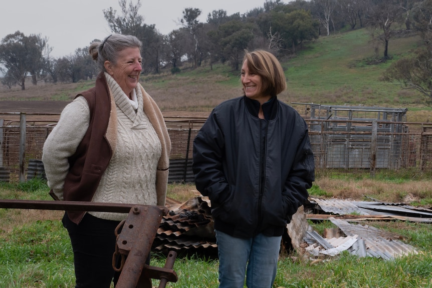 two woman stand very close together, looking to the right of the frame.