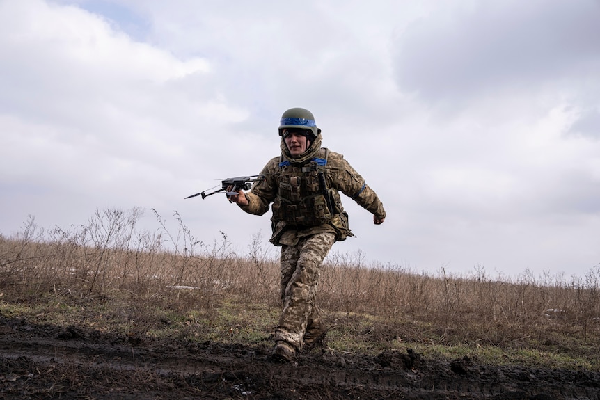 A soldier runs with a small drone over an open field. 