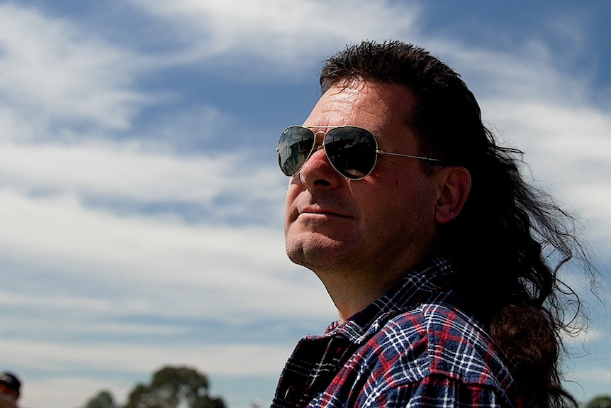 A man wearing sunglasses and sporting a mullet. 