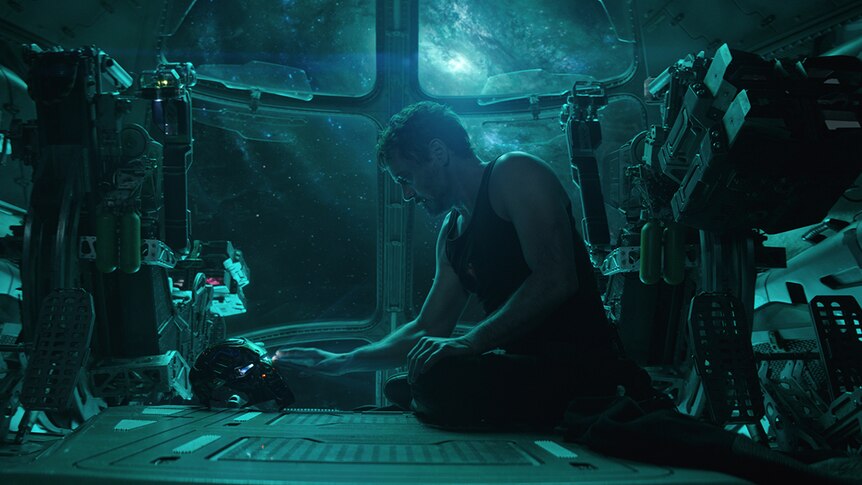 Colour still of Robert Downey Jr. sitting alone in spacecraft touching Iron Man mask in 2019 film Avengers: Endgame.