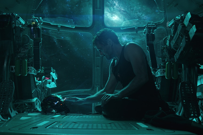 Colour still of Robert Downey Jr. sitting alone in spacecraft touching Iron Man mask in 2019 film Avengers: Endgame.