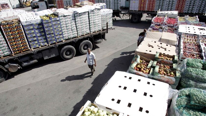 A Palestinian man walks near trucks loaded with fruits and vegetables
