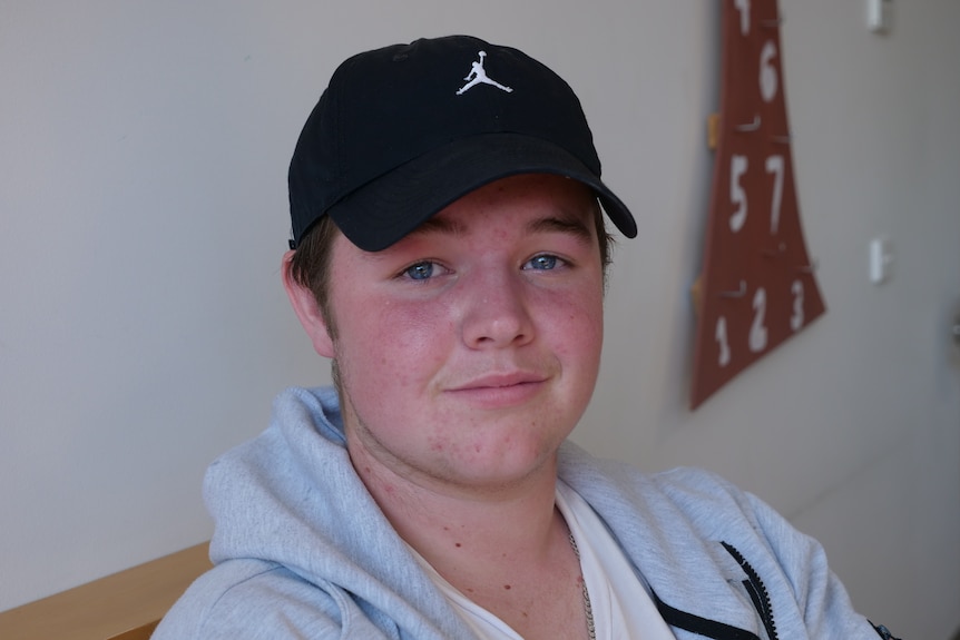 A teenage boy sitting down wearing a cap