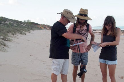 Three volunteers stand near a turtle nest dug in the sand on Cable Beach, Broome.