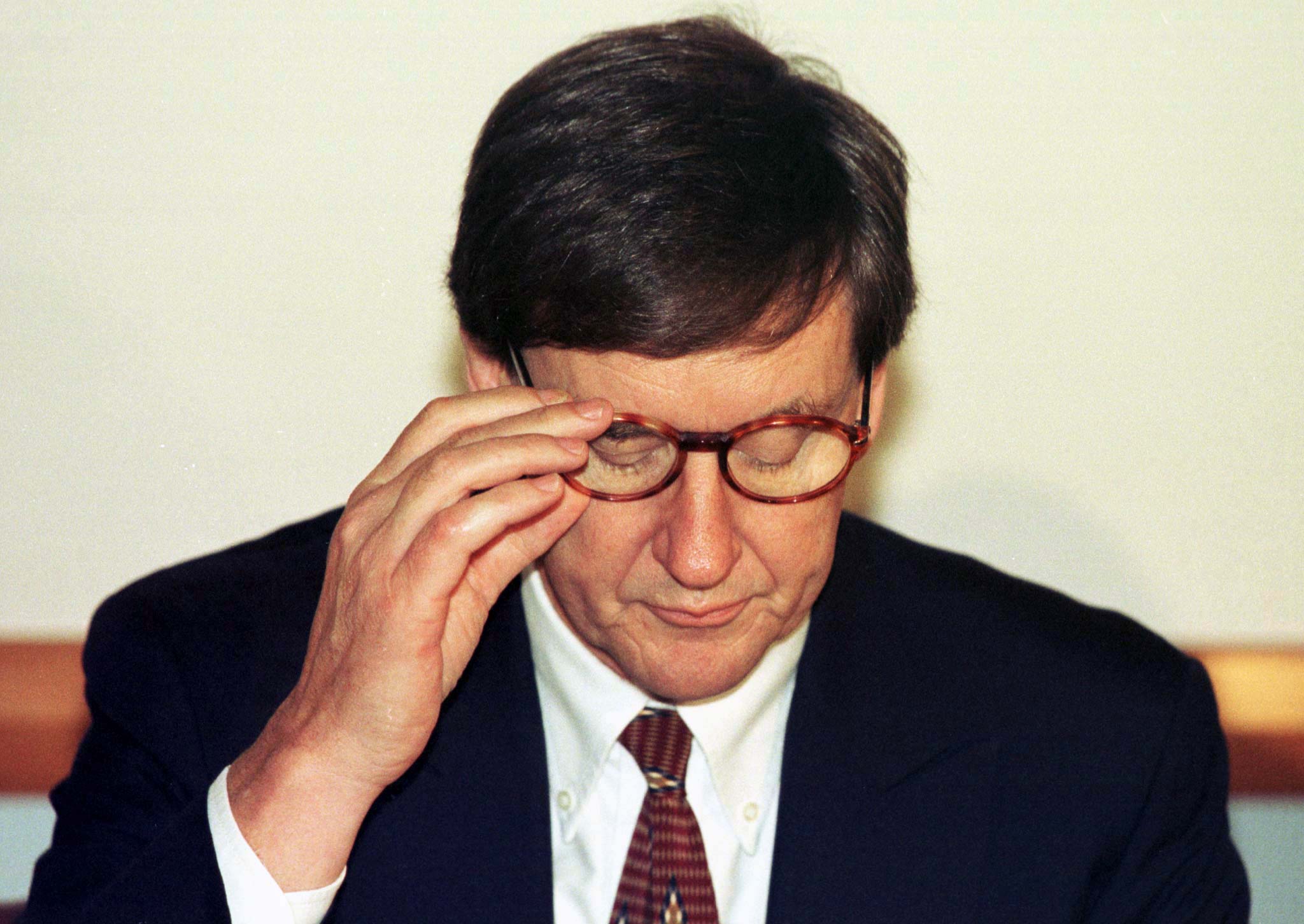 An older man wearing glasses looks down at his notes 