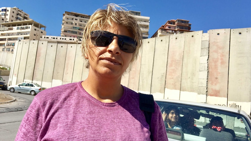 Palestinian woman Suzan, 30, stands in front of a tall concrete barrier that surrounds Shuafat camp in the West Bank.