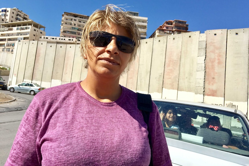 Palestinian woman Suzan, 30, stands in front of a tall concrete barrier that surrounds Shuafat camp in the West Bank.