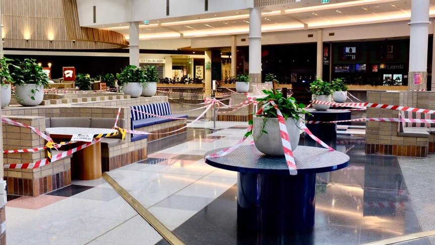 A shopping centre foodcourt is covered with red and white tape, yellow and black tape and a sign saying 'area closed'