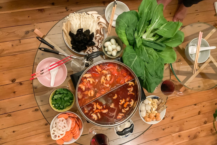 Multiple dishes with food to be placed in a soupy hot pot are seen photographed underneath a lazy Susan, on a wooden table.