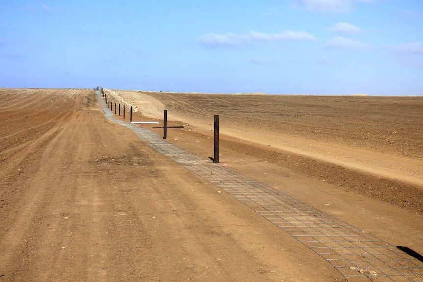 Fencing wire lies alongside new fence posts in a barren paddock.