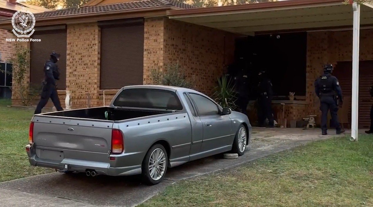  Car out the front of a house with police at the door.