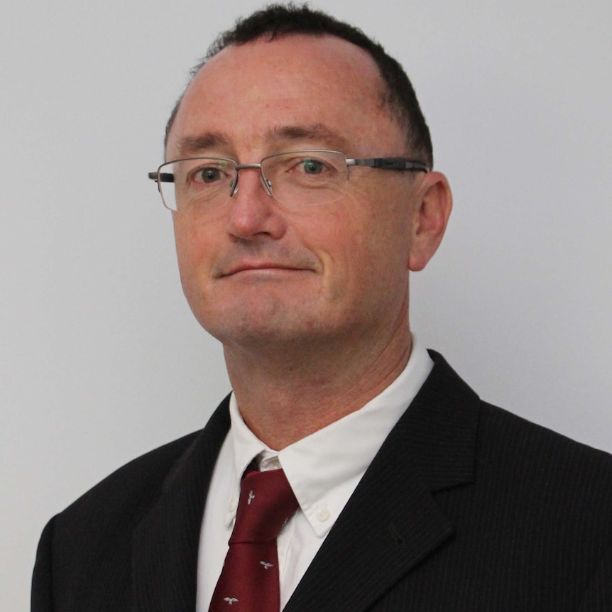 White bespectacled man wearing a suit and suit