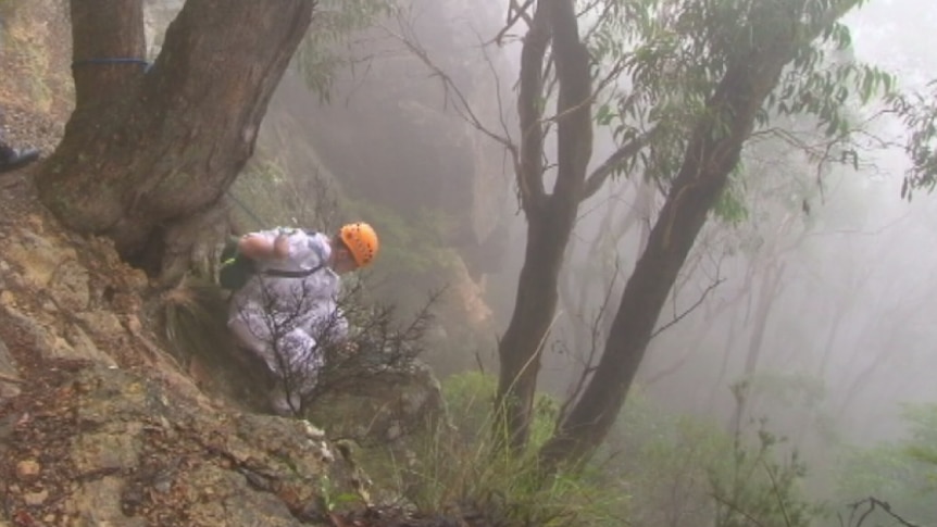A rescue worker tries to reach a woman who fell down a cliff in the Blue Mountains