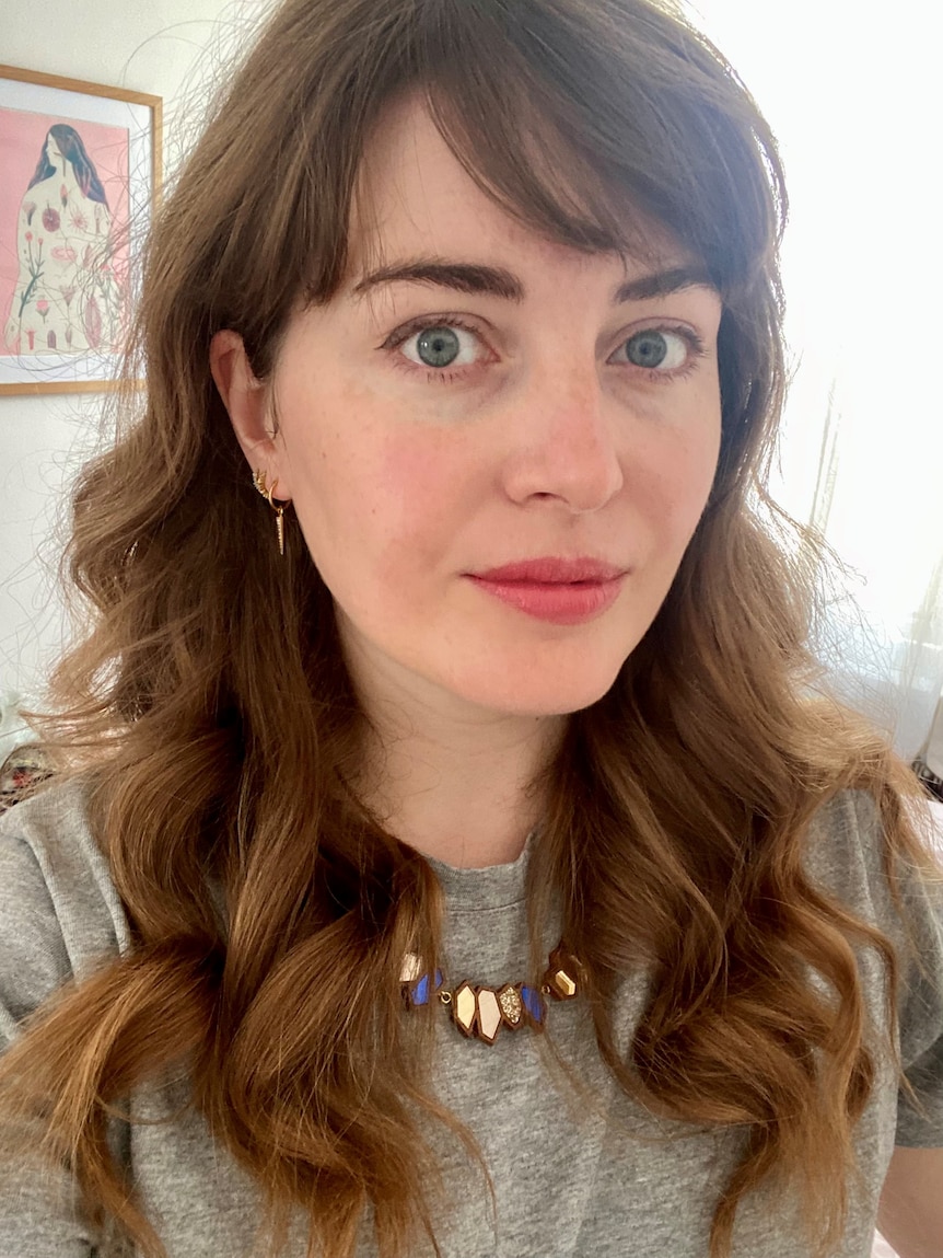 A woman with brown wavy hair and pink lipstick looks at the camera 