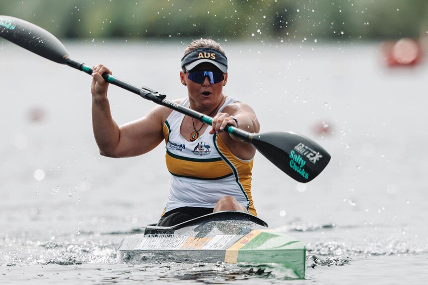 A female kayaker is competing in a kayak, with an intense look on her face. 