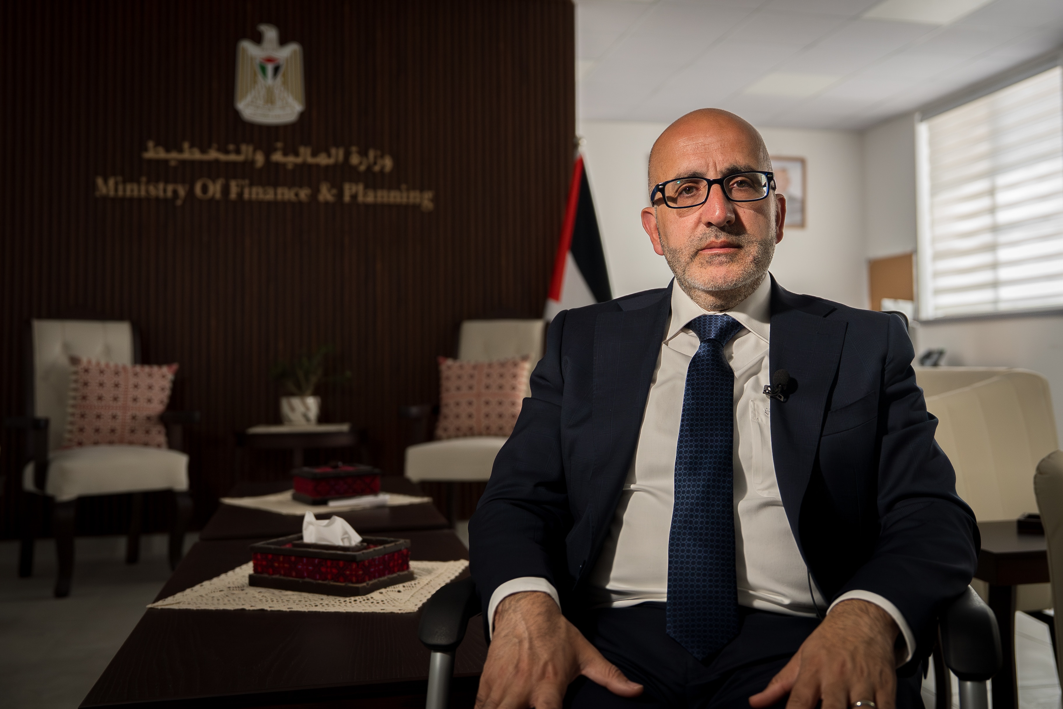 A Palestinian man wearing a dark suit sits in a chair.