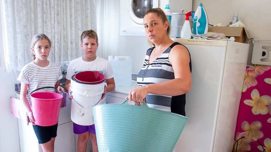 Rebecca Zanatta with her children Jaydon and Macy, hold buckets in the laundry of their home in Stanthorpe.