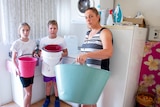 Rebecca Zanatta with her children Jaydon and Macy, hold buckets in the laundry of their home in Stanthorpe.